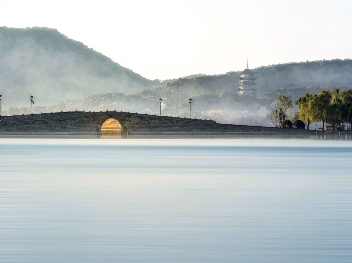A stone bridge over misty West Lake with the Leifeng Pagoda beyond, Hangzhou