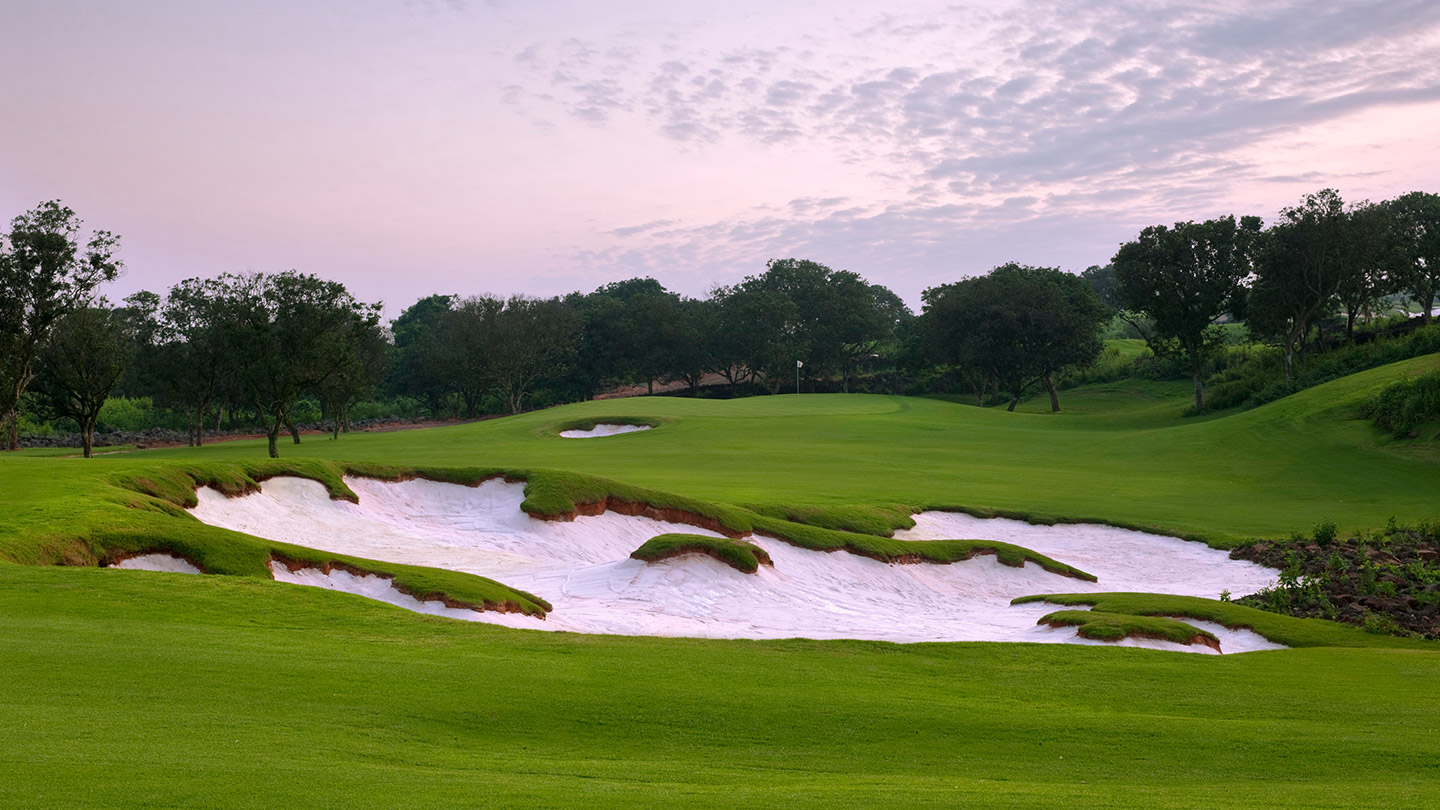 Rugged white-sand bunkers across a fairway at dusk on the Blackstone course, Haikou