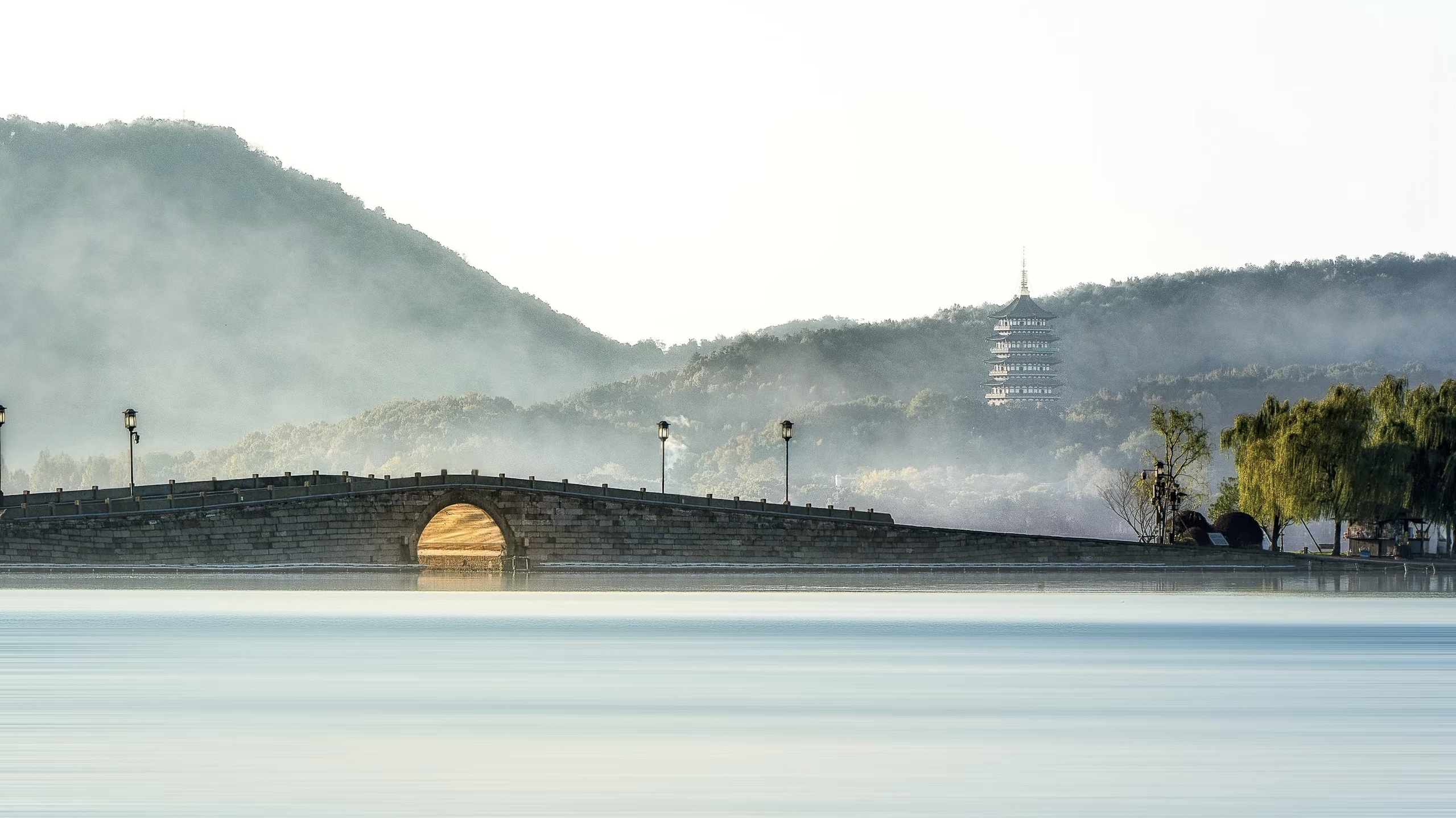 A stone bridge over misty West Lake with the Leifeng Pagoda beyond, Hangzhou