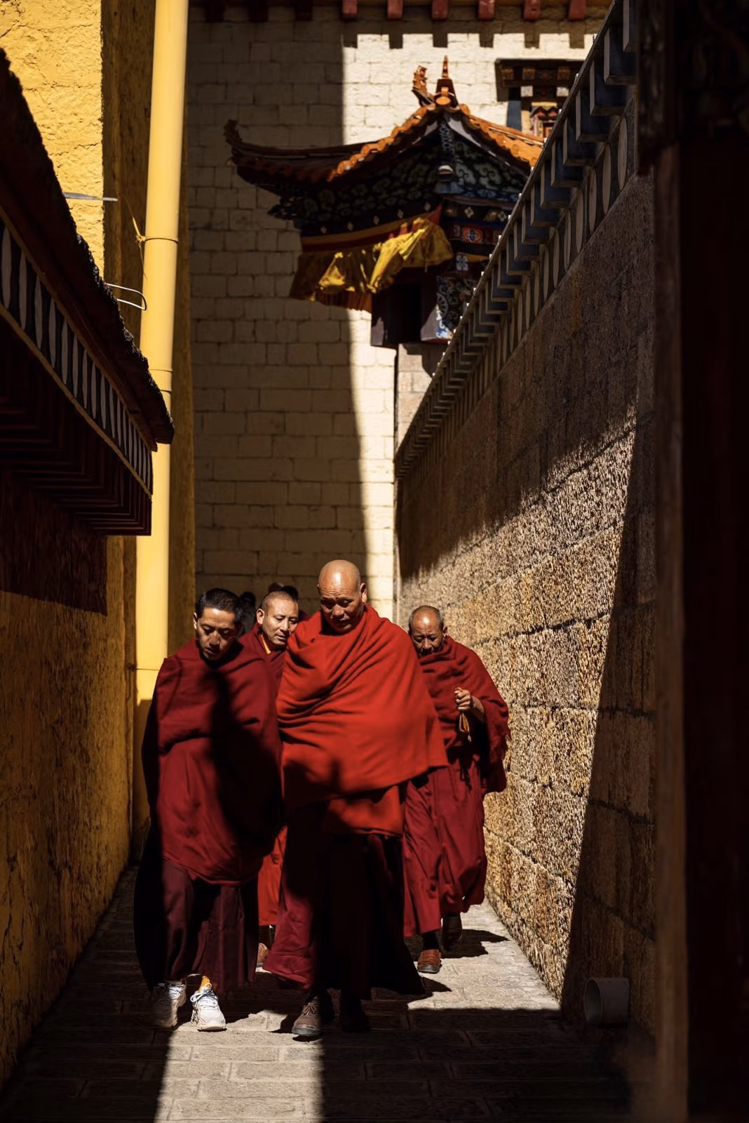 Monks in crimson robes walking a sunlit lane at Songzanlin Monastery, Shangri-La