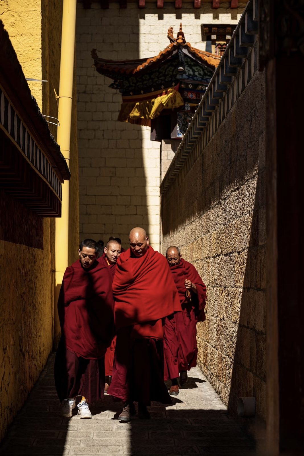 Monks in crimson robes walking a sunlit lane at Songzanlin Monastery, Shangri-La