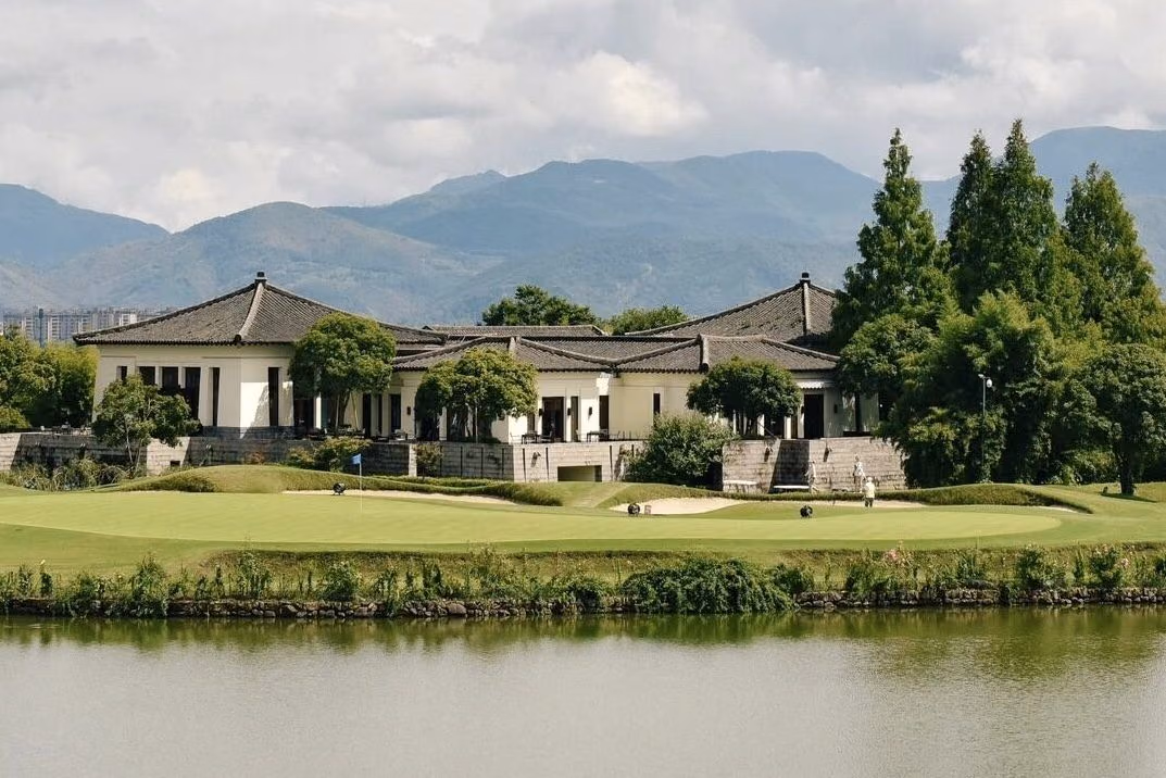 The grey-tiled clubhouse at Fuchun Golf Club across the water behind a lakeside green