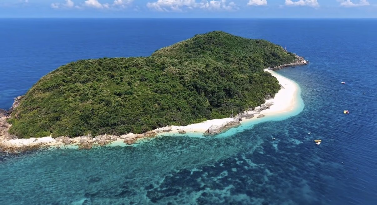An aerial view of a jungle-covered island ringed by white sand and turquoise reef off Hainan