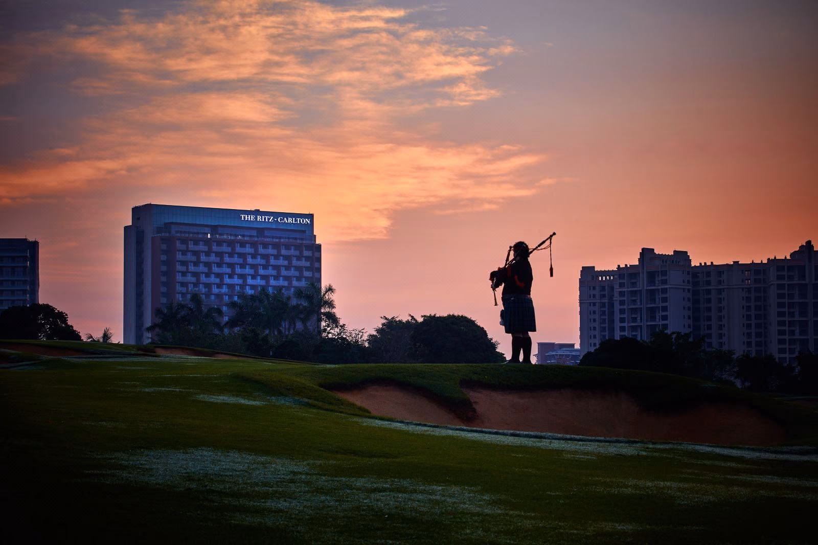 A lone piper at sunset on the fairway beneath The Ritz-Carlton at Mission Hills, Haikou