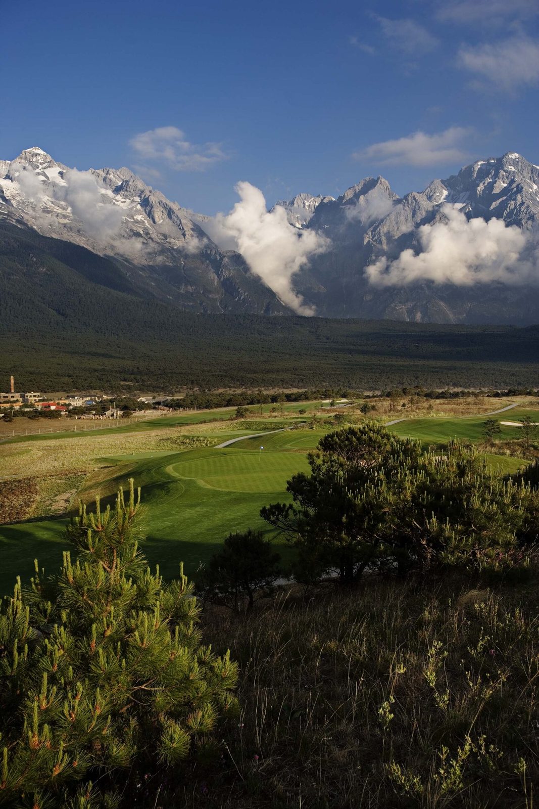 A fairway at Jade Dragon Snow Mountain Golf Club running toward the cloud-wrapped peaks of the massif