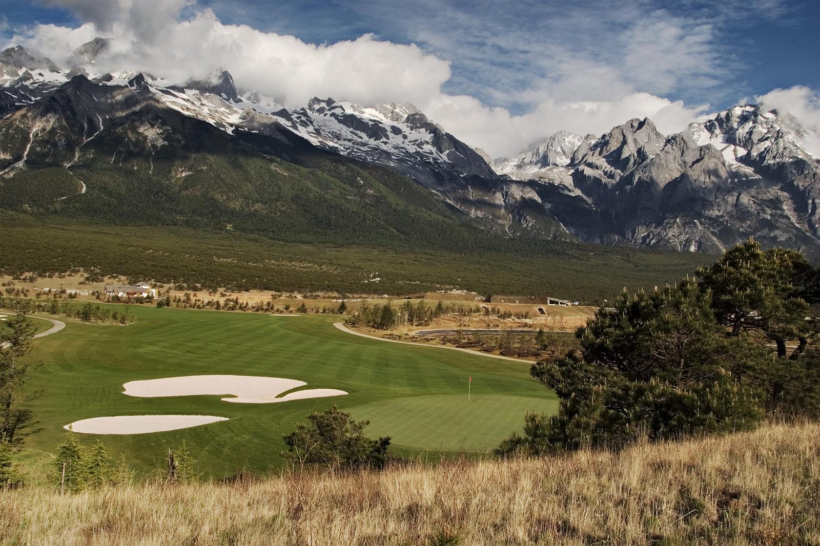 Golden winter grasses framing a fairway beneath the snow range at Jade Dragon