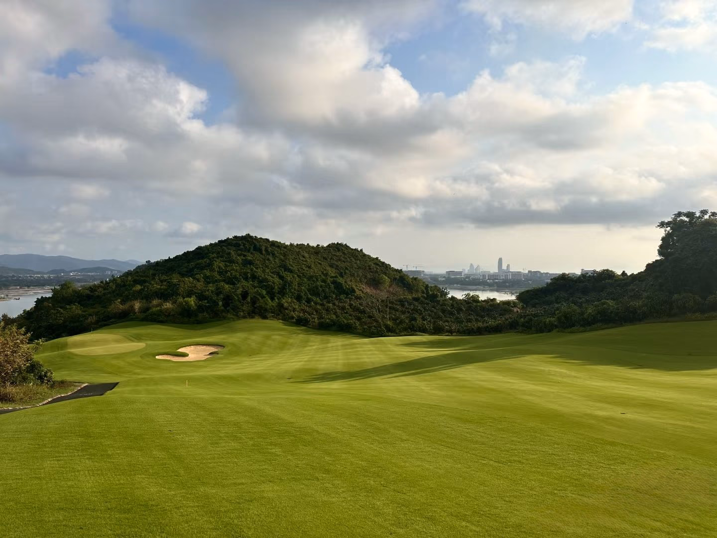 A hilltop fairway at Lu Hui Tou with Sanya's skyline in the distance