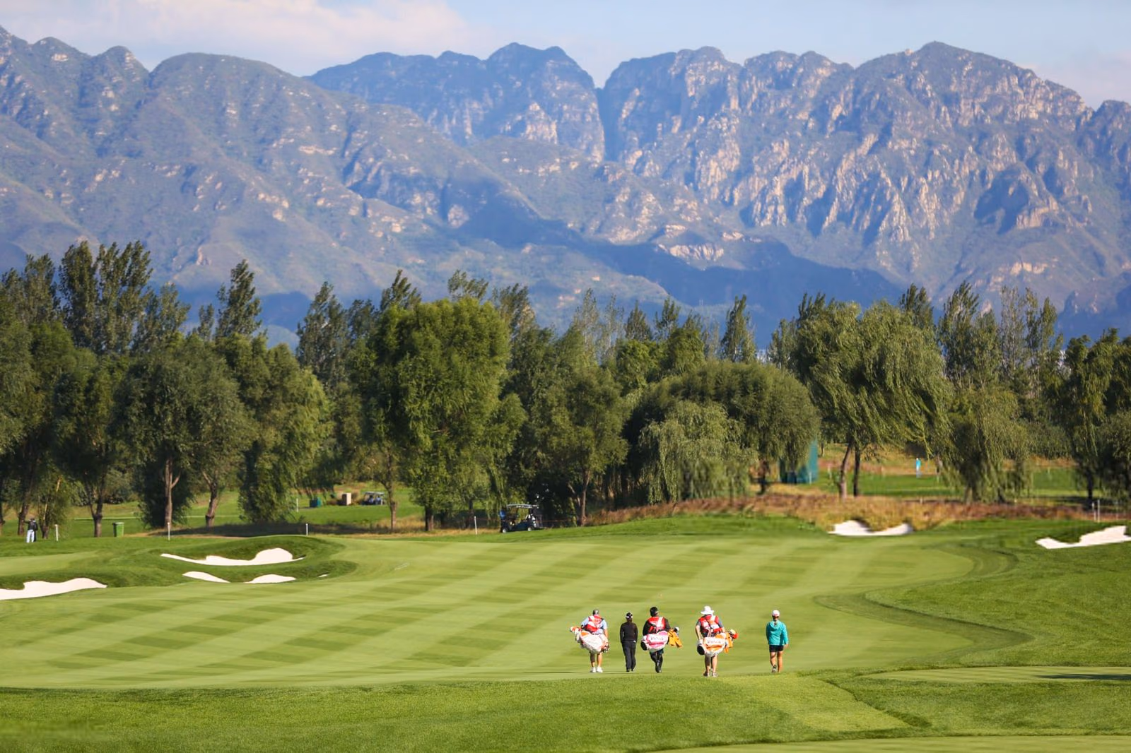 Caddies and players walking a Reignwood fairway beneath the jagged Jundu peaks