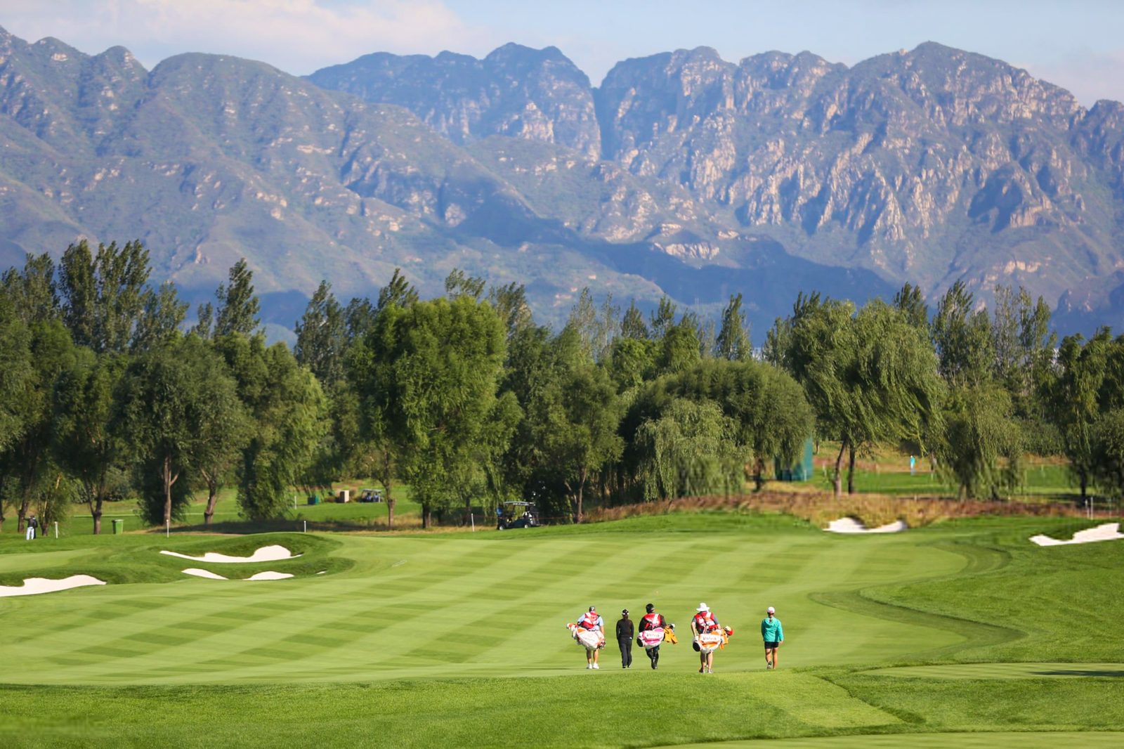 Caddies and players walking a Reignwood fairway beneath the jagged Jundu peaks