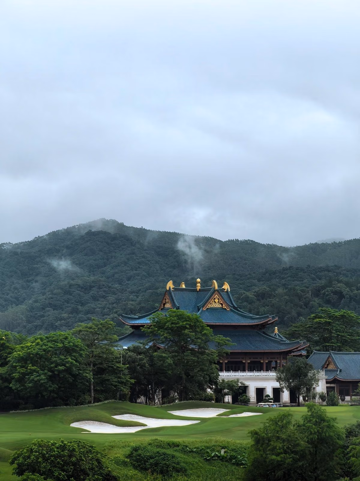 A palace-style clubhouse above bunkered fairways, misty hills behind
