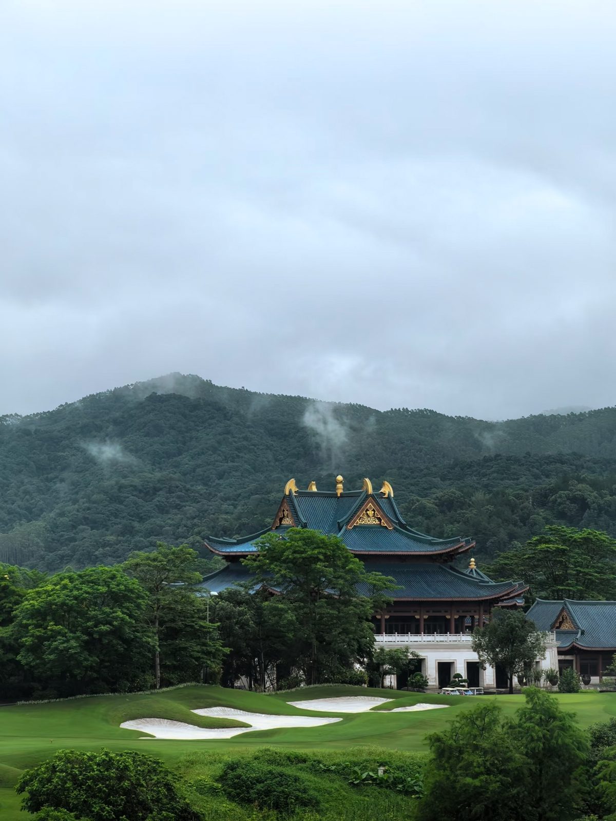 A palace-style clubhouse above bunkered fairways, misty hills behind