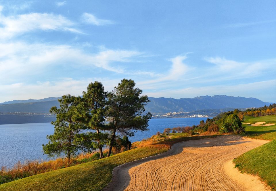 A sculpted bunker curling along the lakeshore at Spring City, mountains across the water