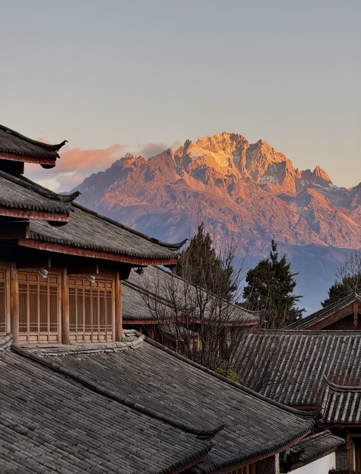 Naxi rooftops in Lijiang with Jade Dragon Snow Mountain glowing at sunset