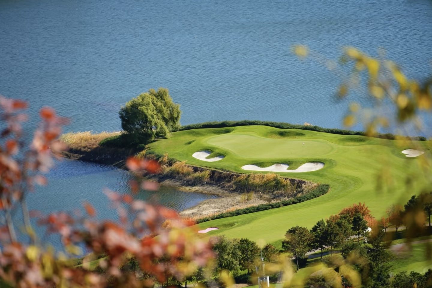 A bunkered lakeside green jutting into Yanqi Lake, framed by autumn leaves